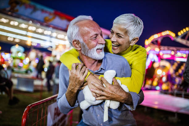 Happy mature couple having fun while piggybacking at amusement park by night.