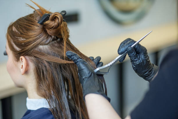 le coiffeur applique la couleur aux cheveux longs. jeune femme dans un salon de beauté. concept de changement d’image, soins capillaires - colorant capillaire photos et images de collection