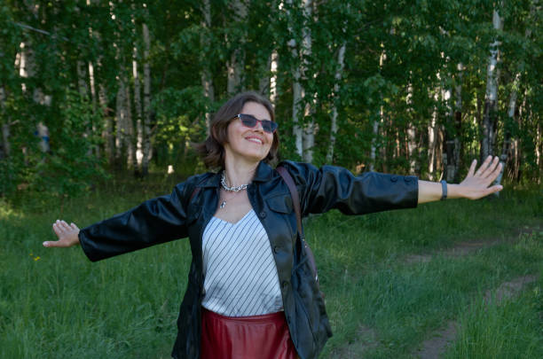 Front view of smiling woman in casual leather clothes with a backpack on forest path