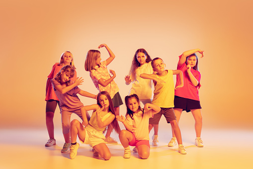 Active and energetic children. Studio shot of dance group of kids wearing casual style clothes posing isolated on yellow background in neon. Concept of music, fashion, art, studying, childhood and ad