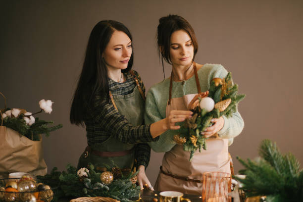 istock Two millennial women making Christmas wreath using pine branches and festive decorations. Small business 1420102330