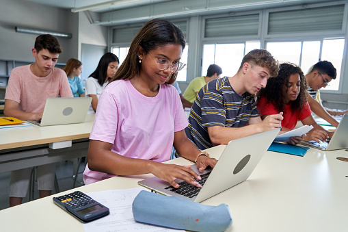 Group of male and female high school students does research in the high school computer lab. The teenage friends enjoy learning and studying together.