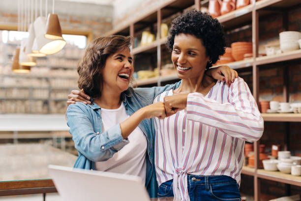 successful ceramists fist bumping each other in their store - verkoopster stockfoto's en -beelden