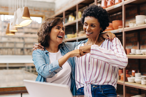 Successful female ceramists fist bumping each other in their store. Two happy shop owners celebrating their achievement as a team. Cheerful young businesswomen running a creative small business.