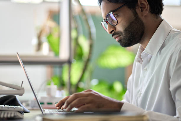 istock Busy indian business man programmer working typing on laptop sitting at desk. 1420106797
