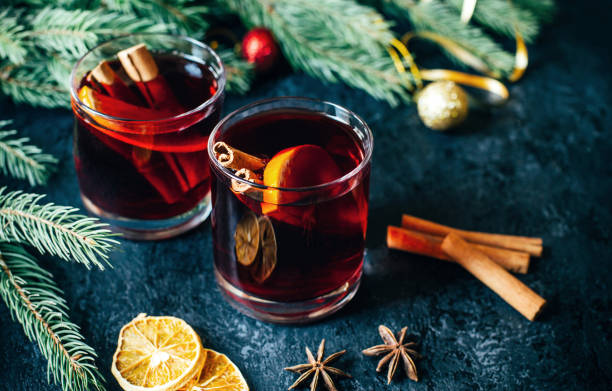 gros plan sur une boisson alcoolisée chaude vin chaud dans deux verres transparents avec un bâton de cannelle, orange et anis étoilé sur une table sombre sur le fond de branches de sapin de noël - fruit winter orange lemon photos et images de collection