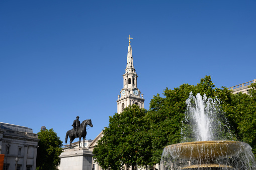 North-east view of fountain (1845), St. Martin-in-the-Fields church, and equestrian statue of King George IV (1828) against clear blue summer sky.