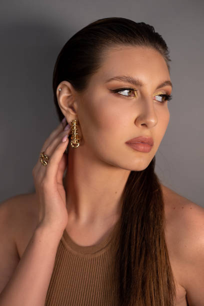 seitenansicht der jungen mysteriösen frau mit langen dunklen haaren, glänzendem make-up, goldenen ohrringen, ring, berührendem hals. - jewelry glamour brown hair stage makeup stock-fotos und bilder