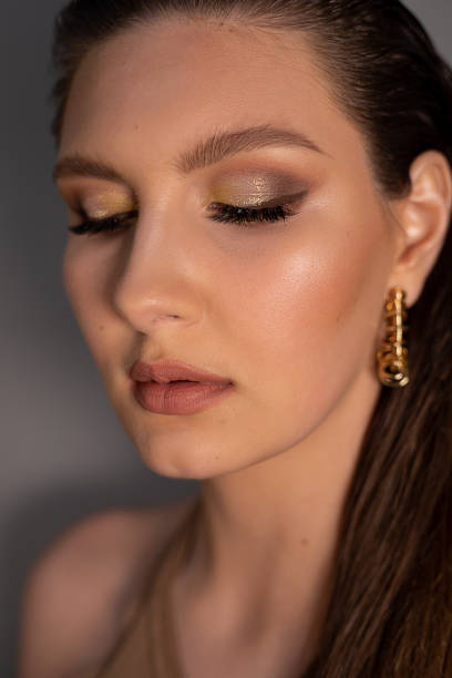 nahaufnahme einer jungen perfekten frau mit hell glänzendem make-up, rosa lippen, mit runden goldenen ohrringen mit geschlossenen augen. - jewelry glamour brown hair stage makeup stock-fotos und bilder