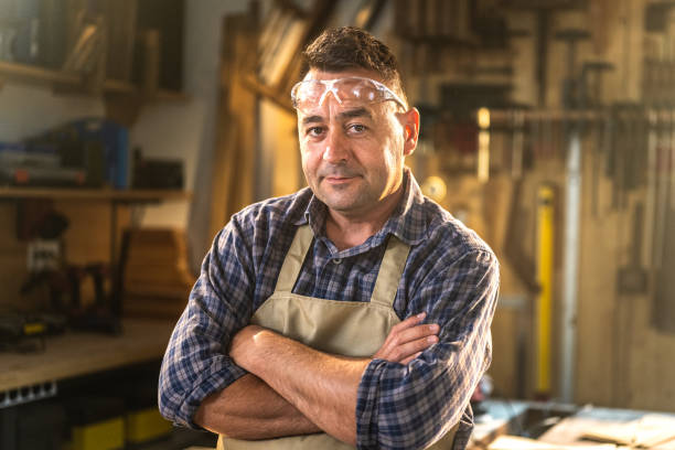 Mature man standing in workshop Portrait of mature male carpenter standing with arms crossed in workshop. rolled up sleeves stock pictures, royalty-free photos & images