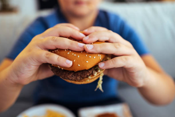 手は食べる前に新鮮なハンバーガーを持っている - overweight child eating hamburger ストックフォトと画像