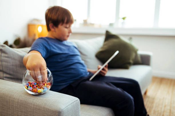 Teenage boy eating candy during e-learning Bored teen guy sitting on sofa while using digital tablet. overweight boy stock pictures, royalty-free photos & images