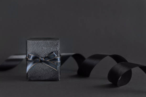 istock Wrapped Black Gift Boxes with a ribbon bow on black close up. Black Friday concept 1420114561