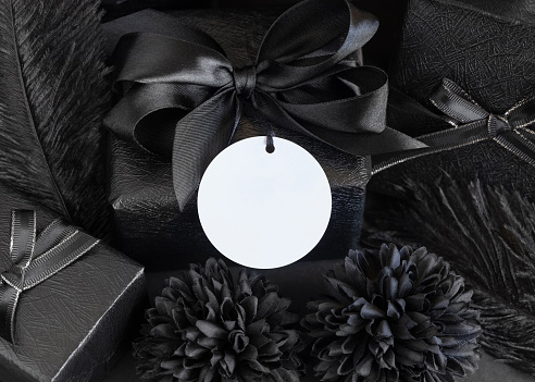 Wrapped Gift Boxes with black paper flowers and decorations and round gift tag, mockup, copy space. Dark composition with blank label card for Birthday, Anniversary or black party present