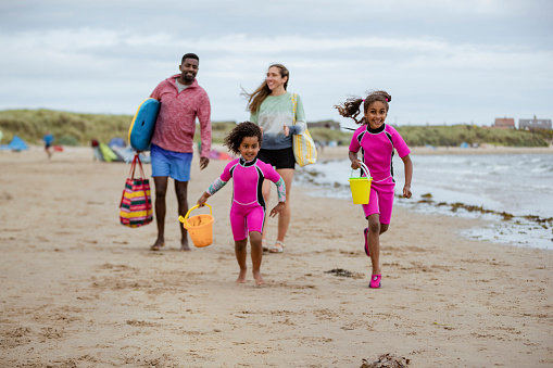 A front-view shot of a family walking on the sand at a beach in Beadnell, Northumberland. They are playing together and they're ready for a fun day.
