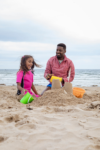 A shot of a father and daughter sitting down on the sand at a beach in Beadnell, Northumberland. They are playing together and building sand castles with beach buckets.