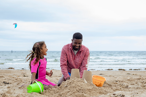 A shot of a father and daughter sitting down on the sand at a beach in Beadnell, Northumberland. They are playing together and building sand castles with beach buckets.