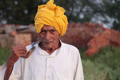 Senior farmer of Indian ethnicity carrying sickle on his shoulder portrait outdoor.