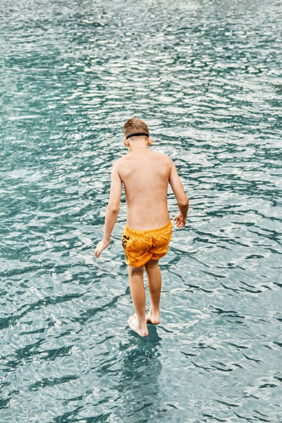 istock Boy jumps from stone pier to sea touching water 1420126605