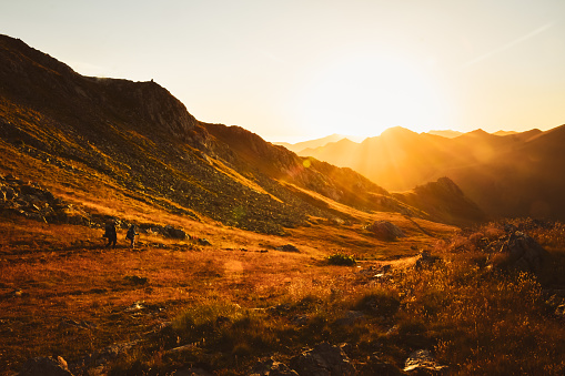 Man and woman hikers in distance hike on trail outdoors on beautiful sunset in autumn together against sun. Cinematic inspirational active people on trek in caucasus mountains