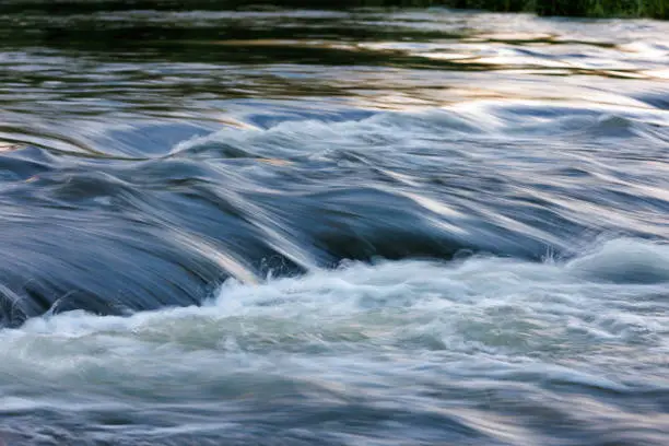flowing water of a summer river with a small rapid waterfall at evening light, long or slow shutter speed, 0.13 sec exposure