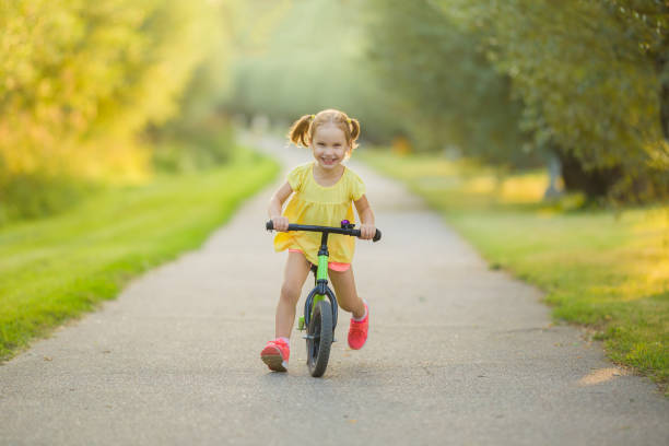 heureuse belle petite fille qui court vite et roule sur le premier vélo sans pédales sur le trottoir du parc de la ville par une chaude journée d’été. mignon bambin de 3 ans. vue de face. apprendre à garder l’équilibre. - 2 3 years photos et images de collection