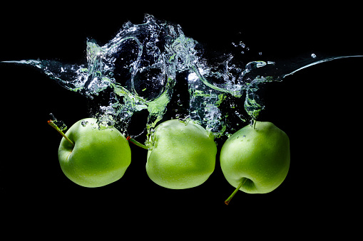 Group of green apples thrown underwater with splashes against black background.