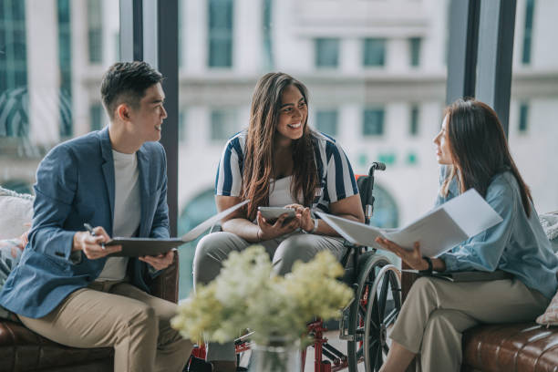 Indian female white collar worker in wheelchair discussion in office lounge with colleague Indian female white collar worker in wheelchair discussion in office lounge with colleague social inclusion stock pictures, royalty-free photos & images