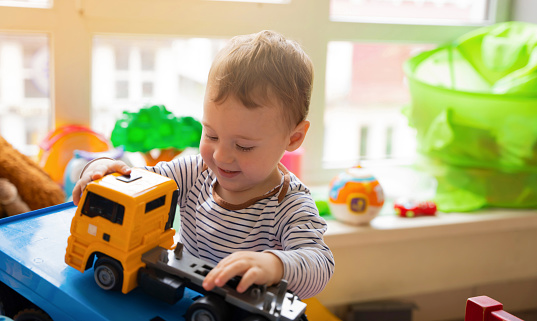 Happy toddler boy plays with car toys in the children's room. Educational toys for young children. Child one and a half years - two years. Selective focus