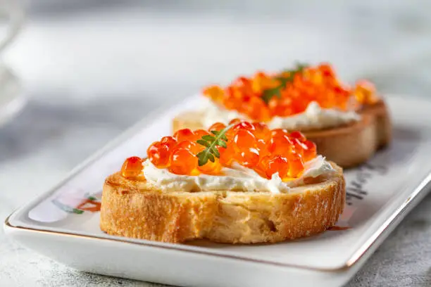 Bruschetta with cheese and red caviar on a plate, close-up