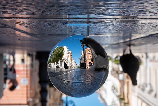 The Main street of the Town of Taranto called Via D'Aquino, in the South of Italy, inside the reflection of a Crystal Sphere on Blurred Background