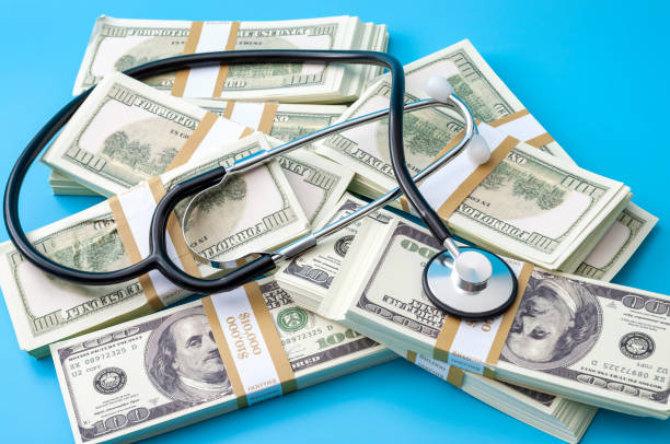 Profit driven hospital, premium medical insurance payment and high doctor bills expense concept with stethoscope, stacks of dollars and no people isolated on blue background Profit driven hospital, premium medical insurance payment and high doctor bills expense concept with stethoscope, stacks of dollars and no people isolated on blue background big pharma stock pictures, royalty-free photos & images