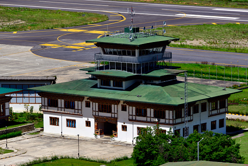 Paro, Bhutan: control tower at Paro International Airport, the only international airport in Bhutan, located in a deep valley on the bank of the river Paro Chhu, with surrounding peaks as high as 5,500m (18,000 ft), it is considered one of the world's most challenging airports, flights operate only in visual meteorological conditions (VMC), an aviation flight category in which visual flight rules (VFR) flight is permitted. Bhutan civil aviation department.