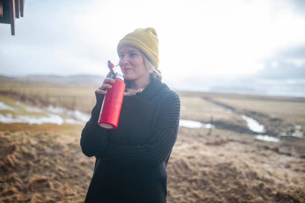 istock A smiling and beautiful woman drinks water from a bottle while standing in a field. ISL 1420148161