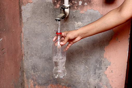 Human hand filling water bottle from the faucet at home.