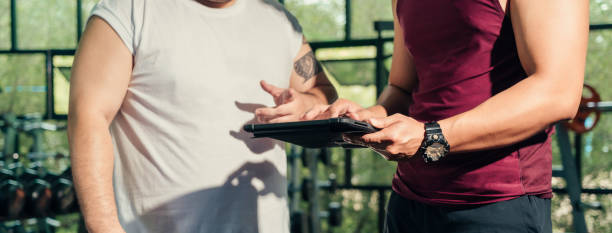 hand des trainers hält und benutzt tablet für den zeitplan und erklärt den fortschritt der männlichen übergröße im loss weight course training. - heavy plant stock-fotos und bilder