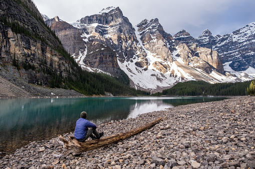 Hiker in Banff National Park. A male hiker sits on a fallen log and admires the beautiful lake and surrounding mountains.