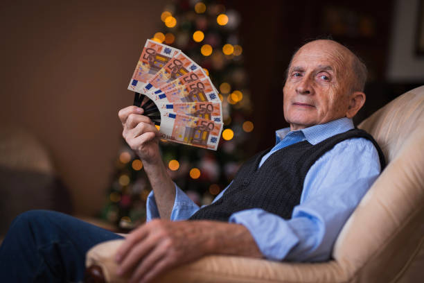 Mature man with fan of money Senior man siting in his chair and holding a lot of money in his hands euro bill in a christmas ornament stock pictures, royalty-free photos & images