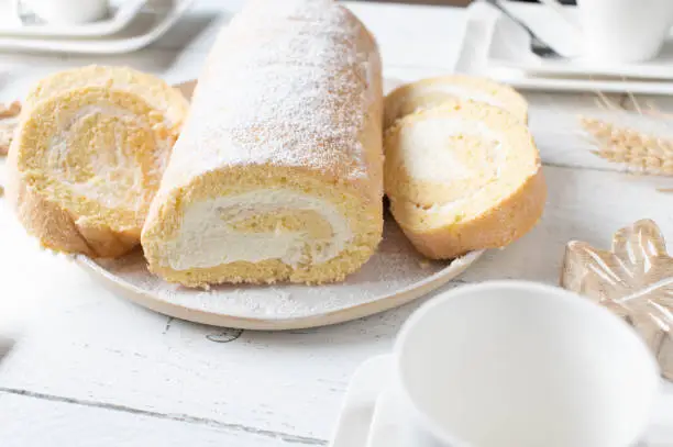 Fresh and homemade baked swiss roll or biscuit roll served with cross section view on a white coffee table.