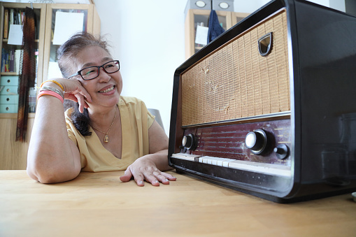The senior Asian woman trying to listen music from the vintage radio.