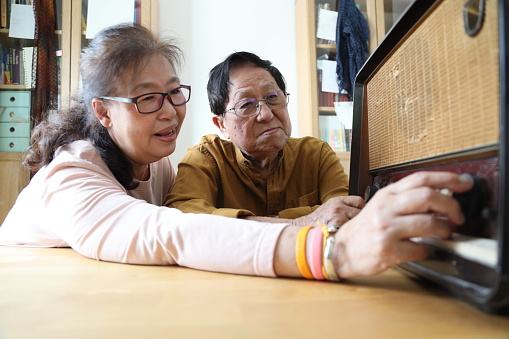 The senior Asian couple trying to listen music from the vintage radio.