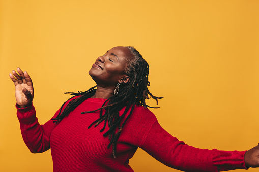 Happy black woman with dreadlocks dancing and having fun while standing against a studio background. Joyful mature woman embracing her natural hair with pride.