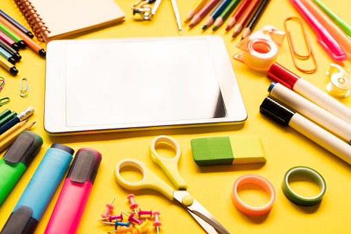 School and office supplies with digital tablet on yellow background