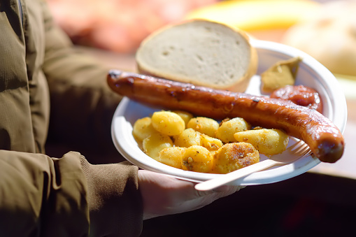 Person buy portion fried potatoes and sausages in disposable plate on famous open air Christmas fair in Krakow. Street food on traditional Xmas market.