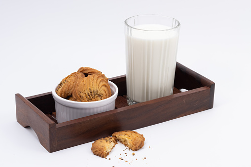 Cookies or biscuits and glass of milk on a wooden serving tray for breakfast or snacks, a healthy concept lifestyle with copy space for text isolated on white background