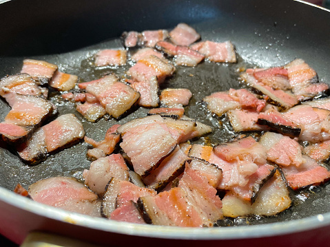 Roasted chopped crispy bacon strips slices in a Hot Skillet frying pan. Fatty junk food, cholesterol