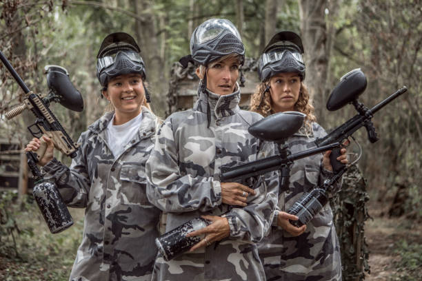 Paintball game, team in camouflage protective uniform with paintball guns and ammunition, strikeball arena battlefield, paintballer aiming and shooting at opponents, airsoft players match tournament