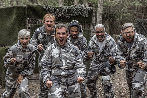 A middle aged mixed race paintball team standing for a team photo on the battlefield
