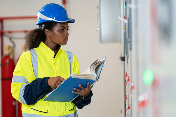 female electrician engineer maintenance electric system with manual book in control room. african american electrician female engineer checking electric system in control room - instruction manual imagens e fotografias de stock