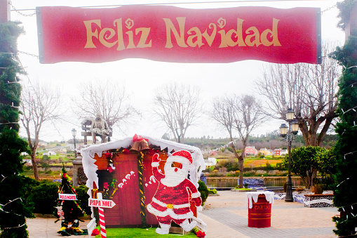 Happy Christmas and Papa Noel sign, figurine and hut, Christmas decorations in public park. Children Playground. Navia, Asturias, Spain.